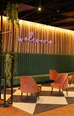 A lobby with a neon pink welcome sign on the wall.